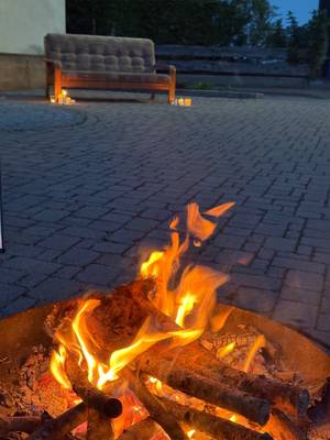 In Vordergrund sieht man ein kleines Lagerfeuer. Im Hintergrund steht ein Sofa mit Kerzen links und rechts.